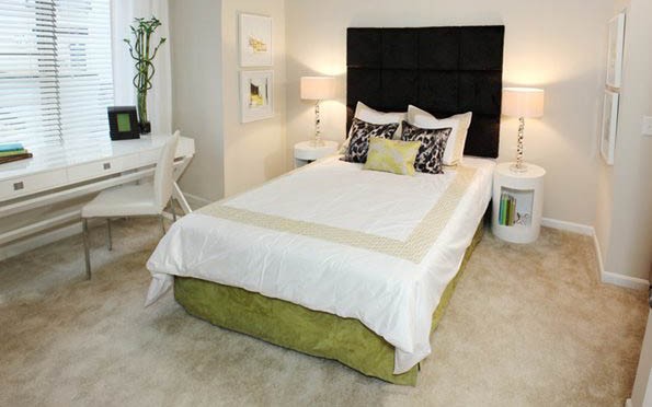 A single bedroom in a U Square apartment. There is a window with horizontal blinds on the left. IN the center of the room is a bed with bedside tables and lamps.