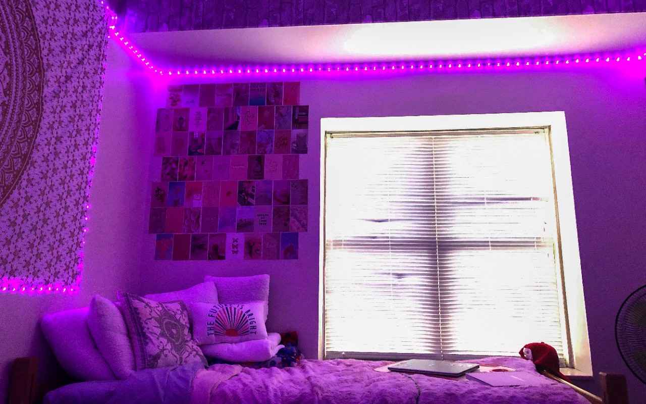Purple lights surround a twin bed with wall decorations. A window is to the side of the bed. 
