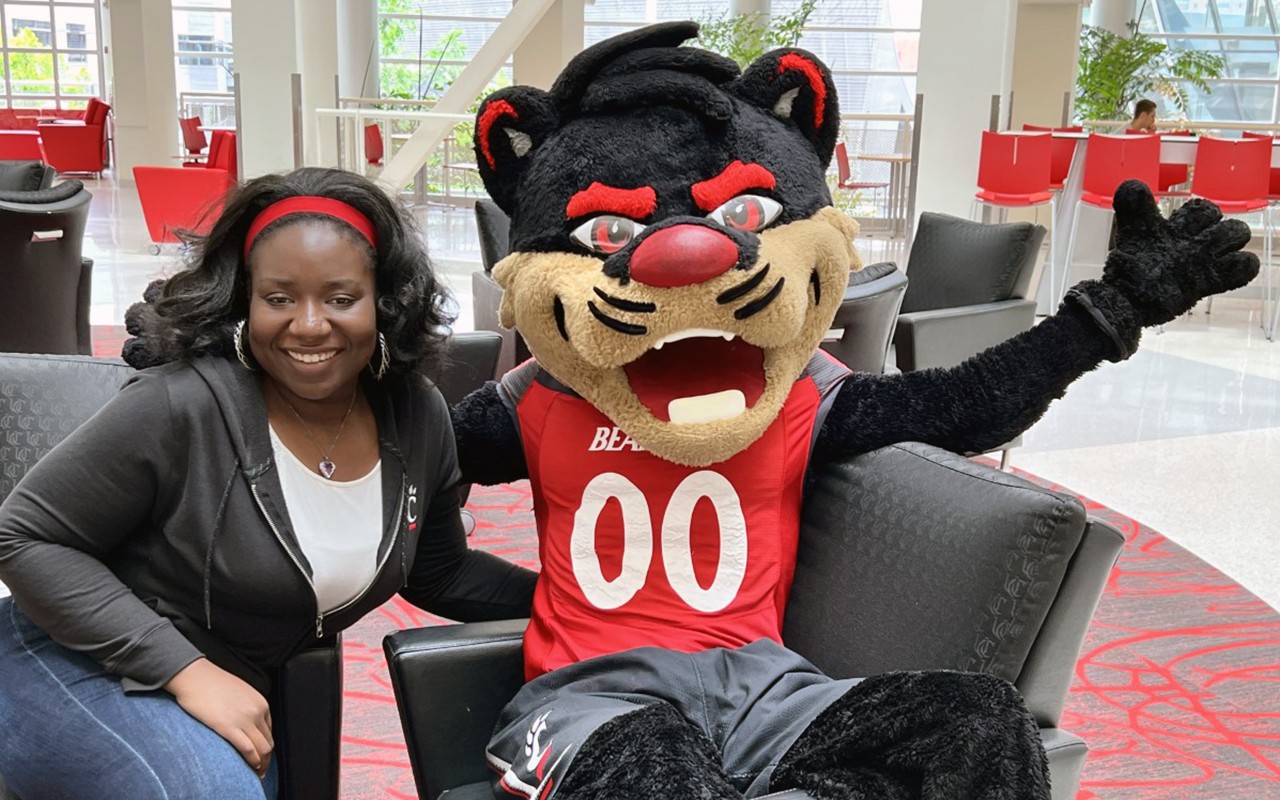 Smiling female African American student seated next to Bearcat mascot