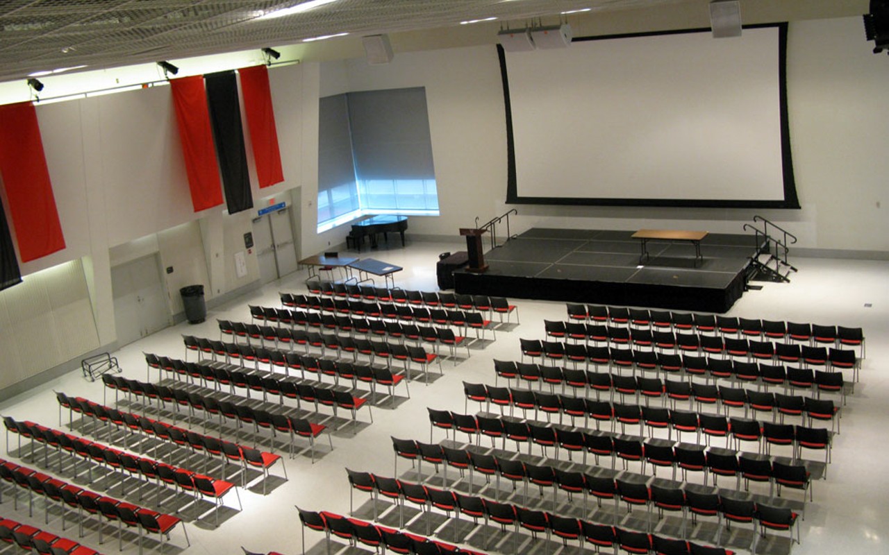 Overhead view of chairs in rows, lecture style with large screen at front of room; banners hang from high walls.