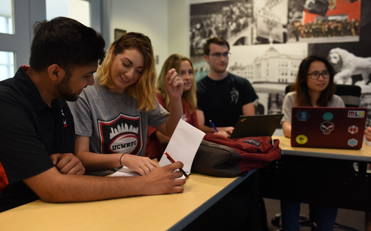 A group of five students sit around a table talking and studying