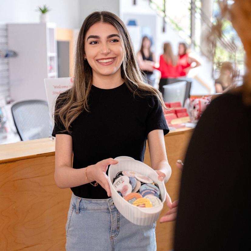 Student holding out a bowl of decorative buttons smiling