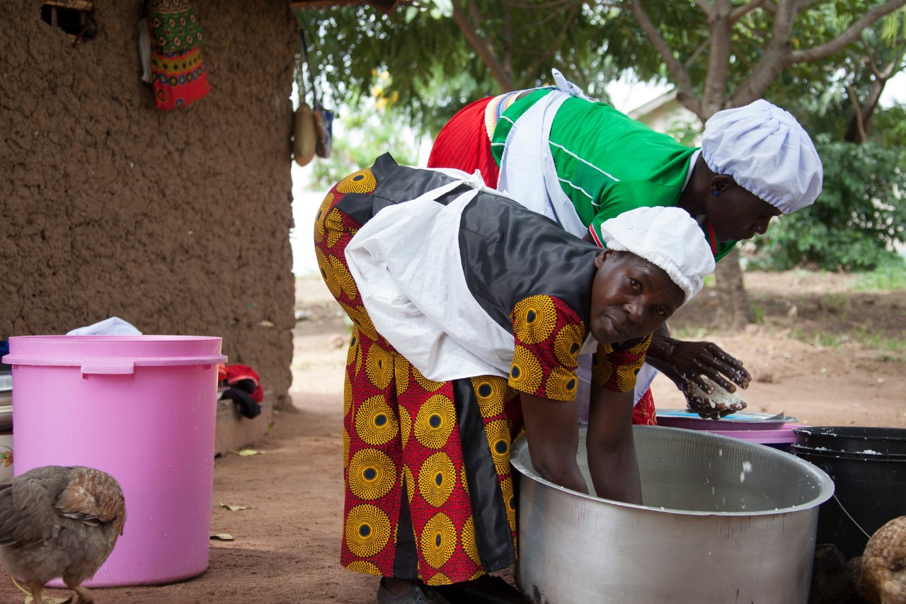 A Tanzanian women stirs rice in a large pot with her hands