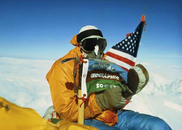 Climber at the top of Mount Everest holding American flag