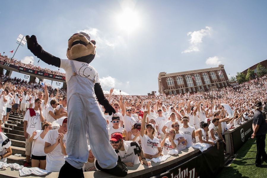 Bearcat mascot in white overalls poses in front of a crowd wearing white