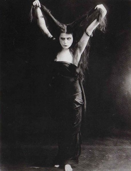 Actress Theda Bara holding her long hair up above her head