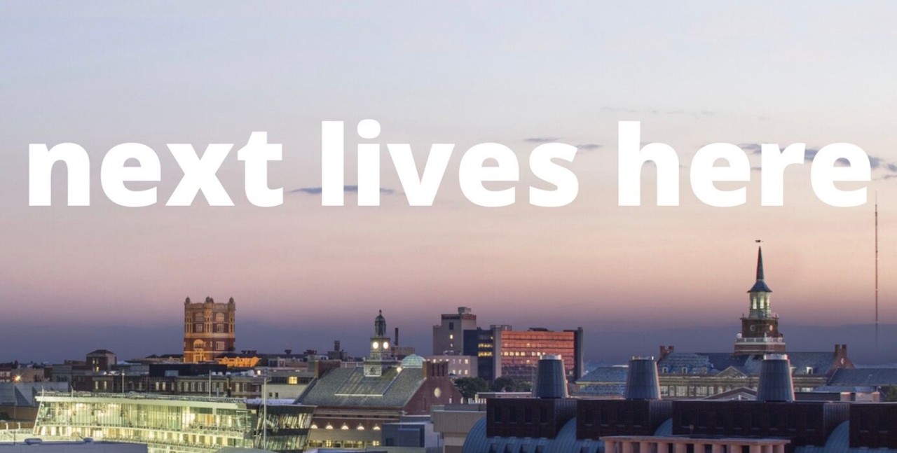 Text reads "Next Lives Here," campus shot in background