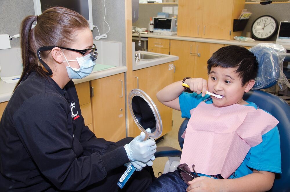 A UC dental hygiene student helps a child clean his teetj
