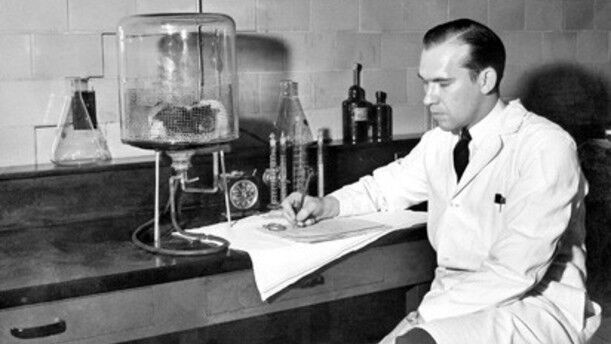 Black and white photo of a man in white lab coat sitting at desk