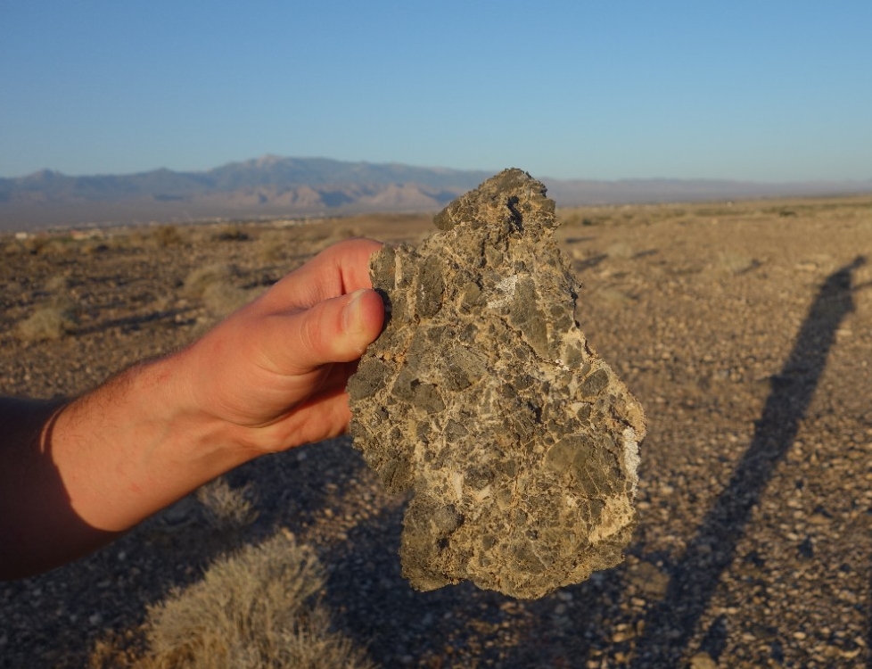 A hand holds a rock deposited at the base of a mountain in a landslide.