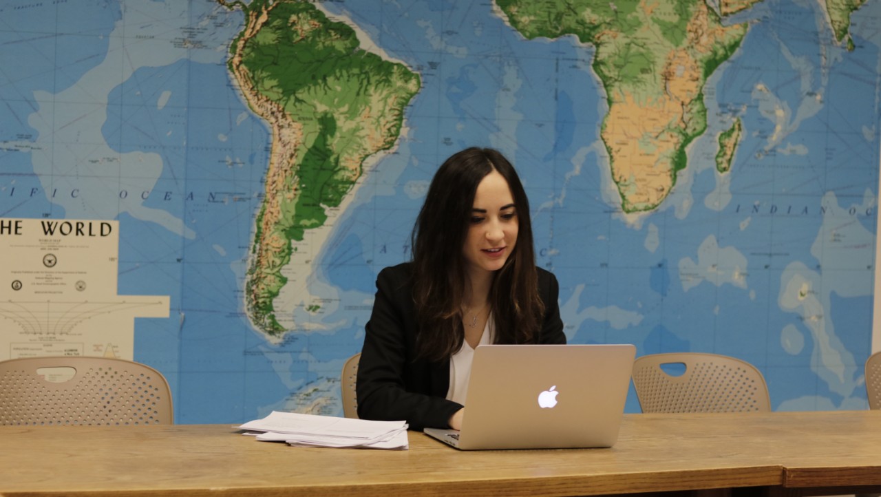 LLM student smiling in front of world map.