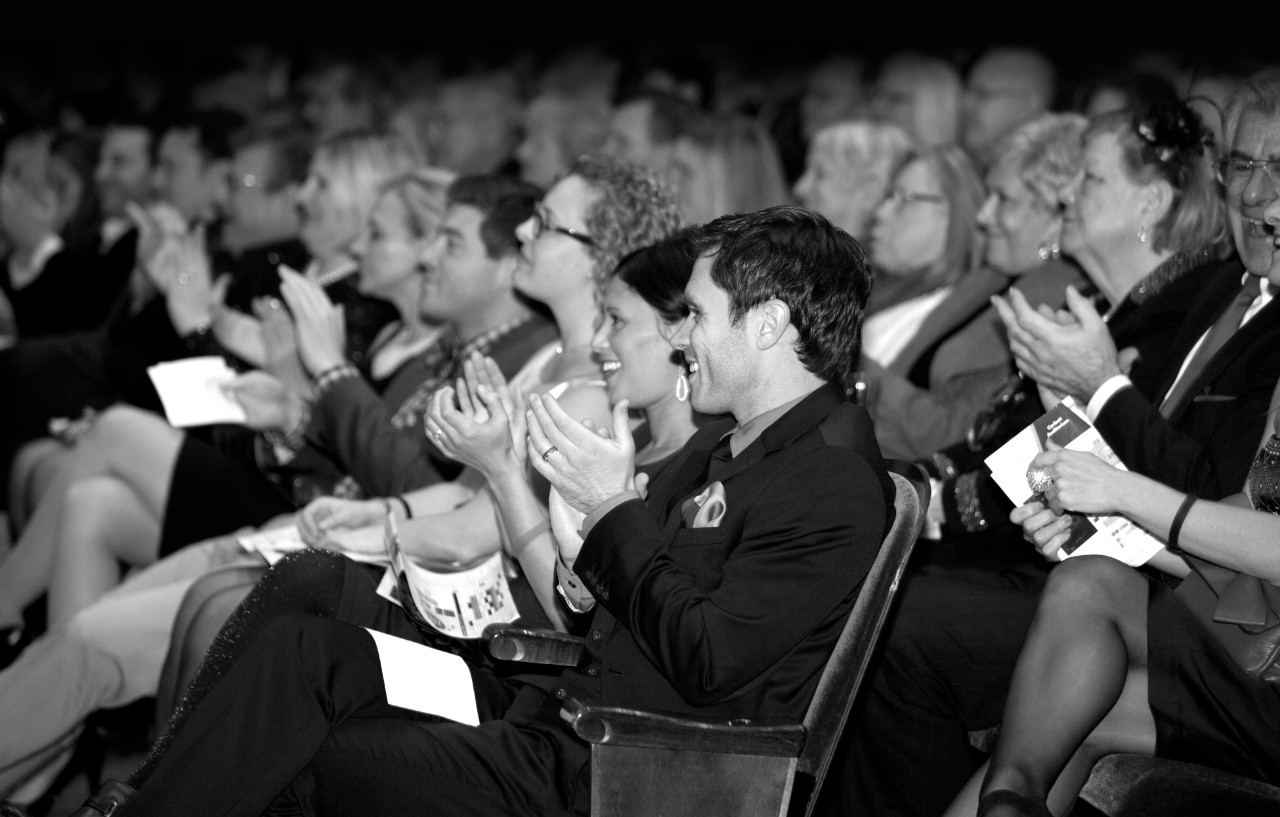 A black and white photo of seated audience members applauding in CCM's Corbett Auditorium.