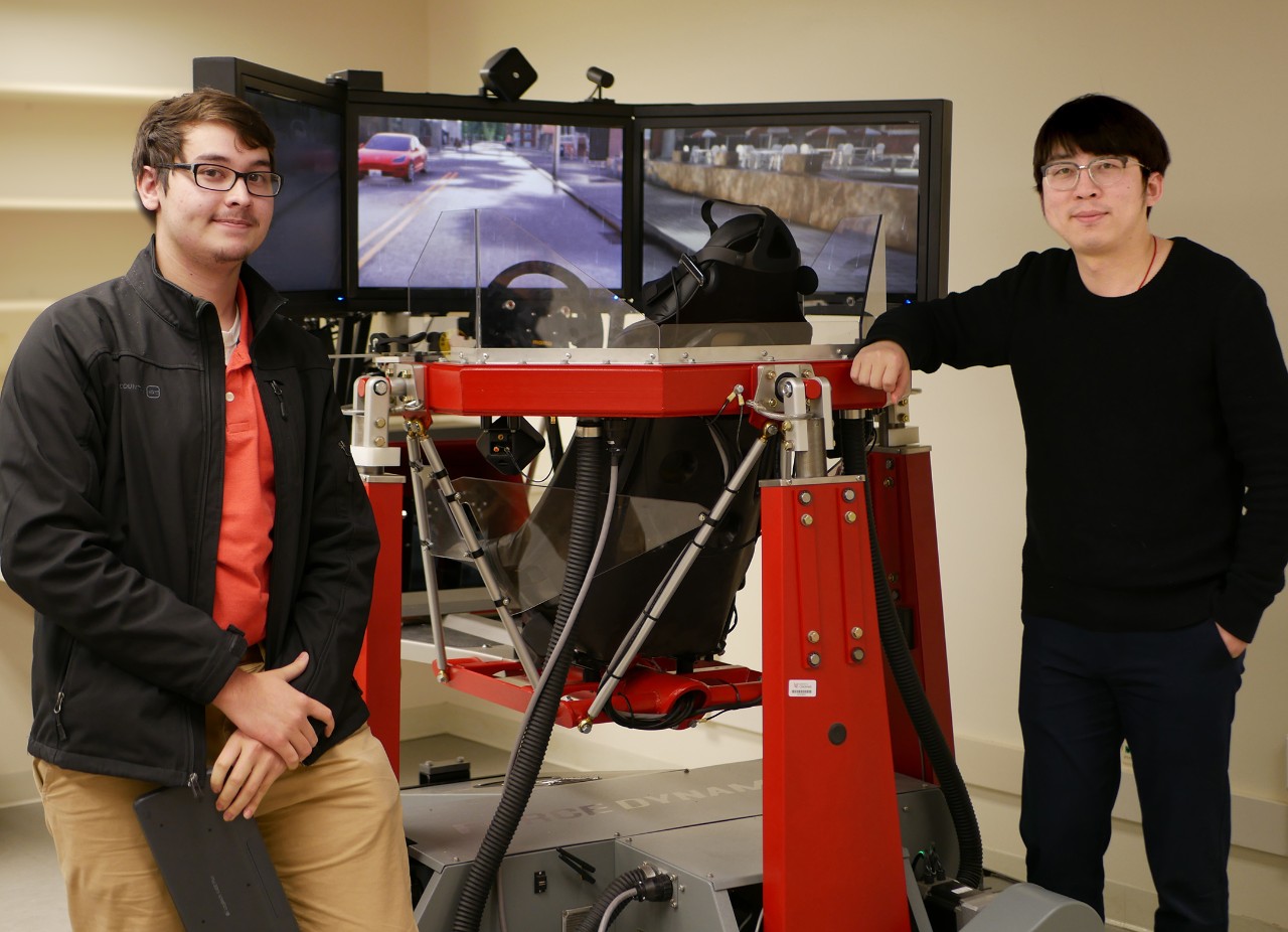 Ma and UC student Andrew Greer stand beside the simulator