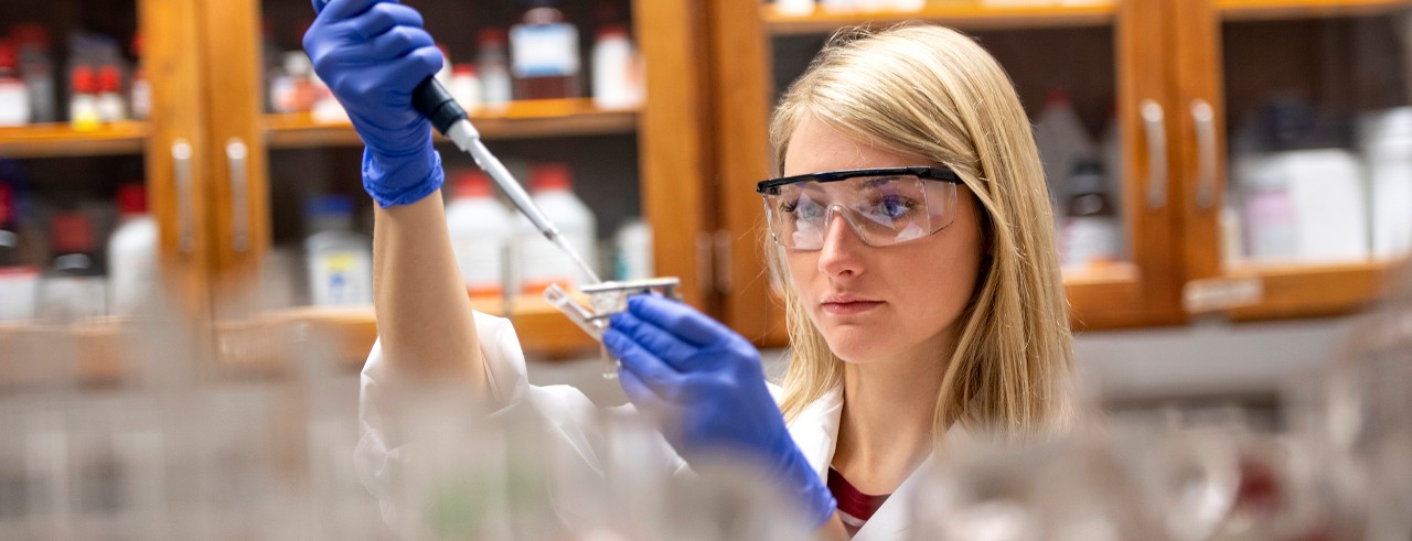 Cosmetic scientist Stephanie Ventura Morris, wearing a white lab coat, working with a beaker and liquid in a lab