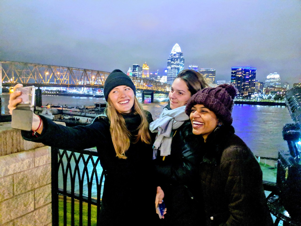 Thre women take selfies with the Cincinnati skyline in the background.