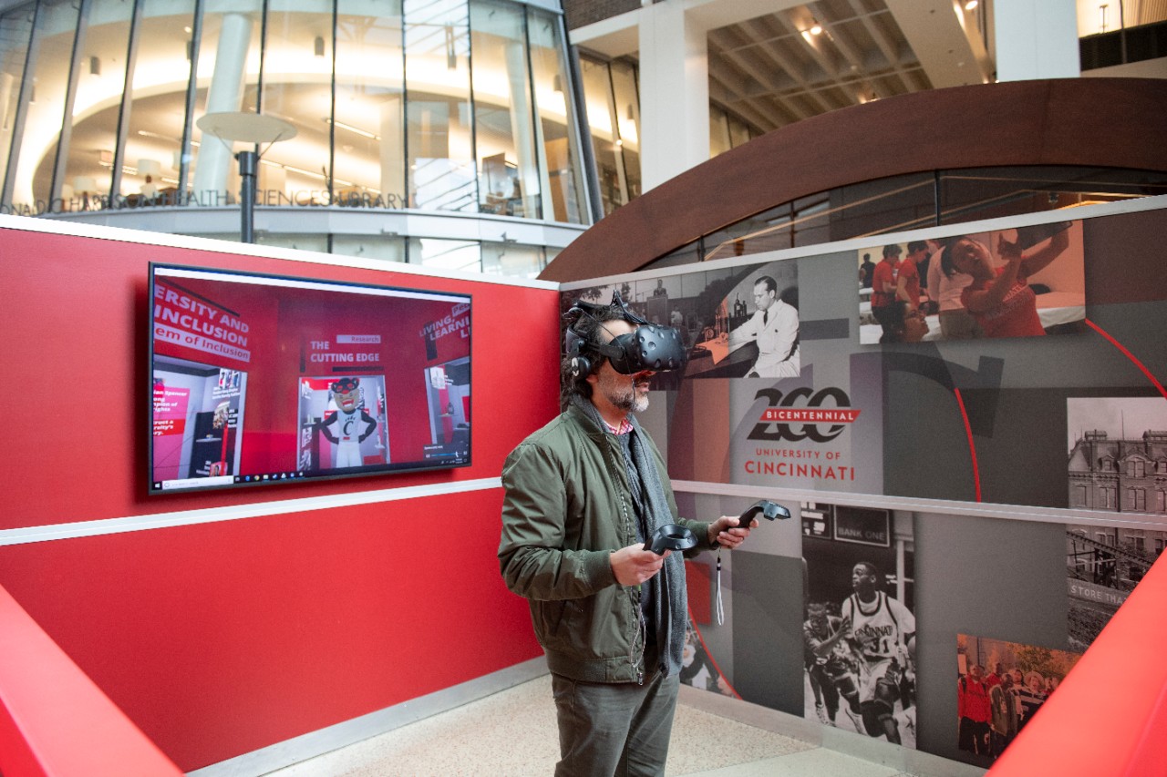 Man wears virtual reality headset and handheld controllers in a booth