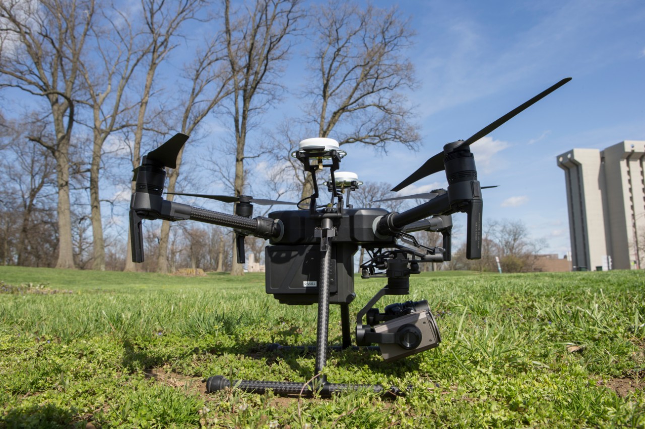 a large black quad copter drone sits outside on the grass on a clear sunny day