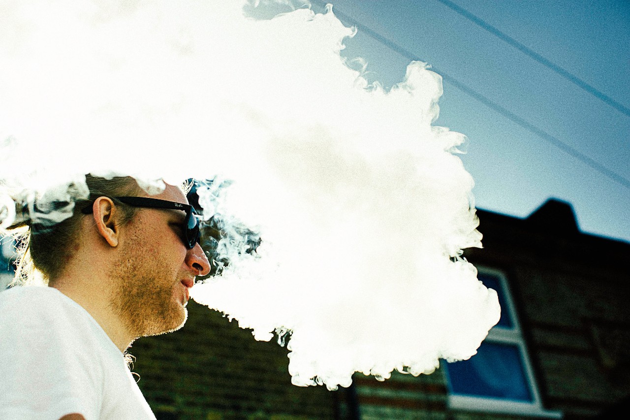 A young man exhales a thick cloud of vapor