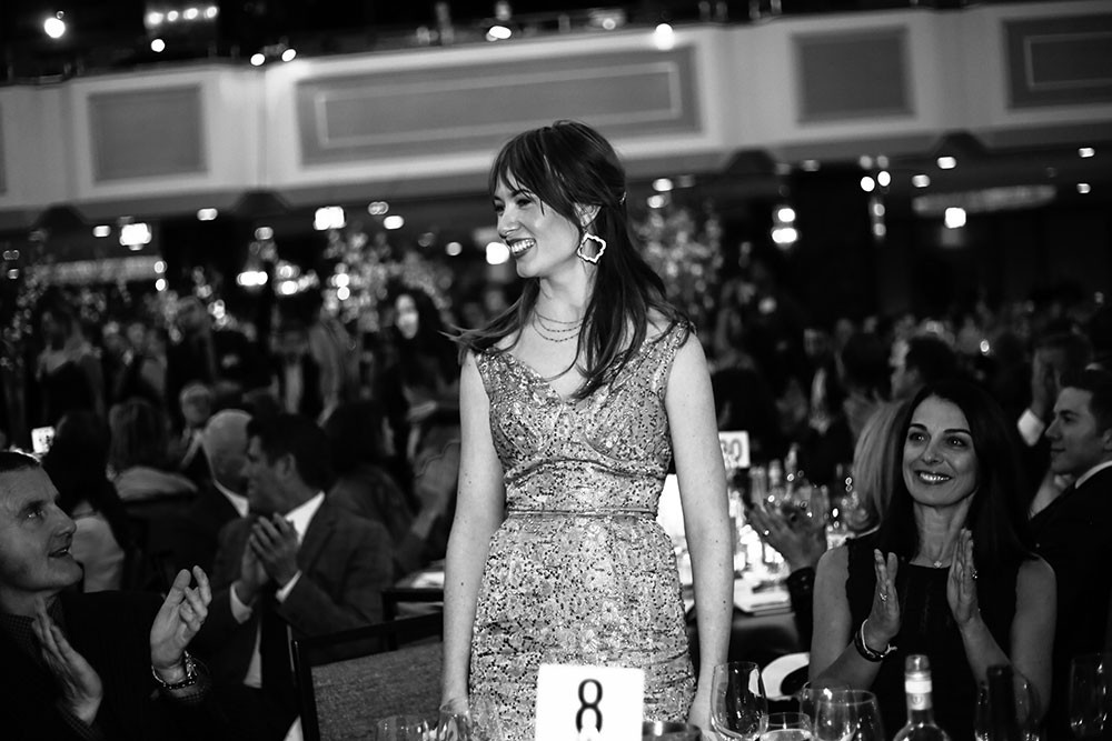 Student in dress smiles graciously and stands in large room at event