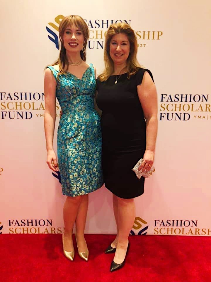 Two women in dresses on the red carpet in front of a Fashion Scholarship Fund backdrop