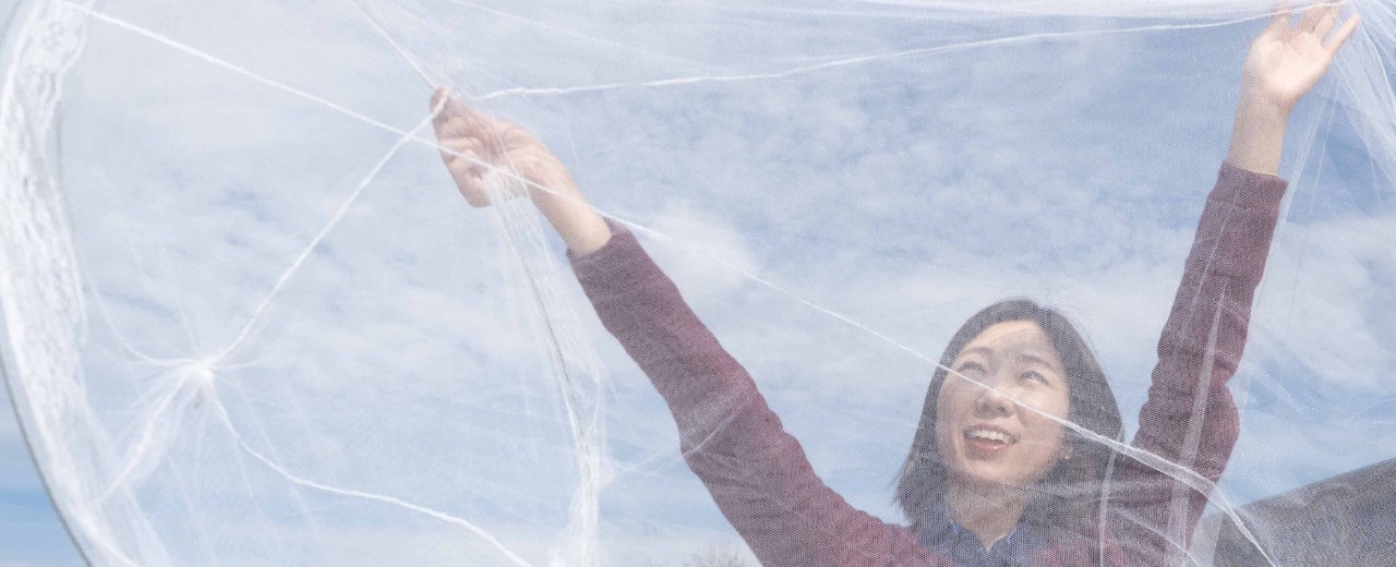 UC student Hana Kim stretches a bed net up to the sky with both hands.
