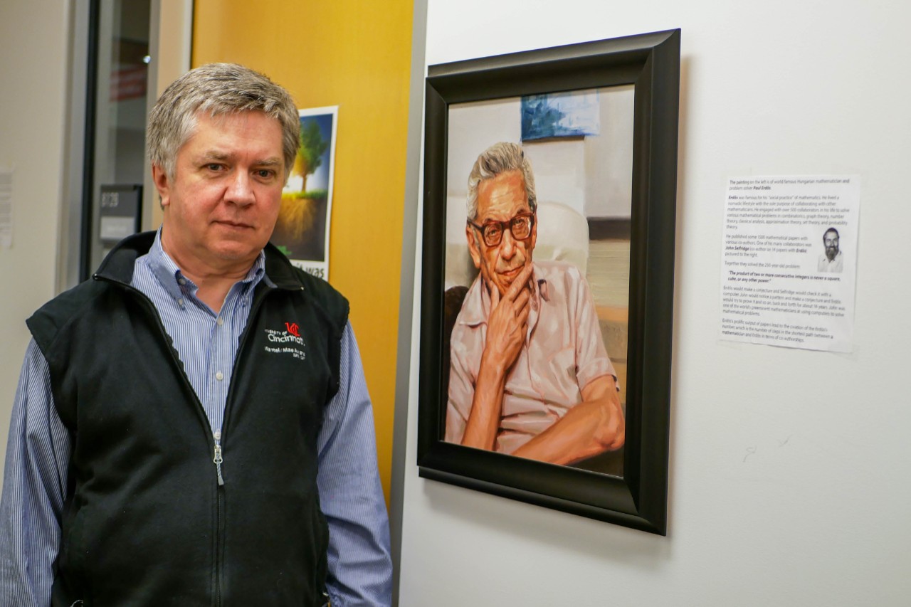 Cahay stand s in office next to portrait of Paul Erdos