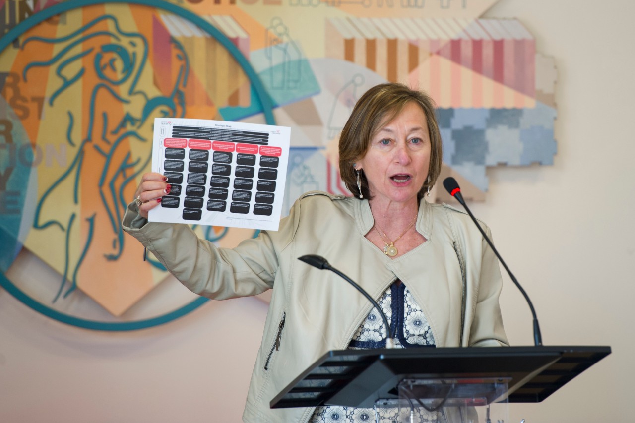 College of Nursing Dean Greer Glazer speaking at a podium holding a copy of the strategic map for the college.
