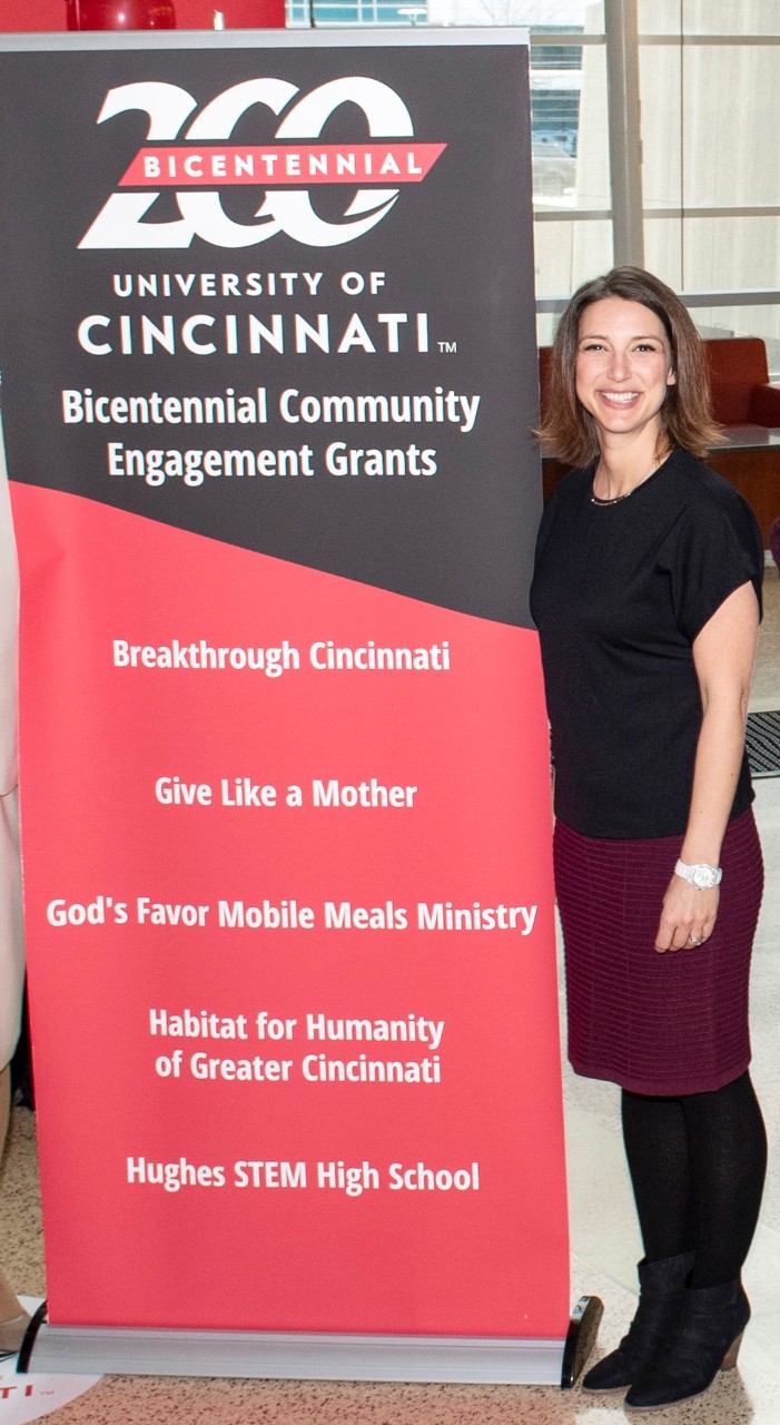 Amy Vann standing next to a banner announcing Give Like a Mother as one of UC's Bicentennial Engagement Grants