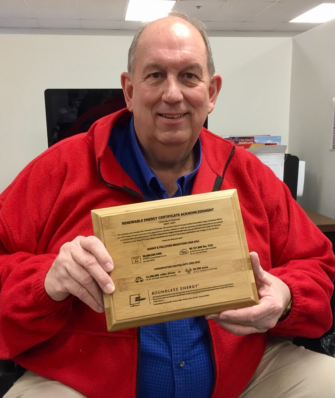 Man holds a wooden plaque with energy renewal credits listed on the front.
