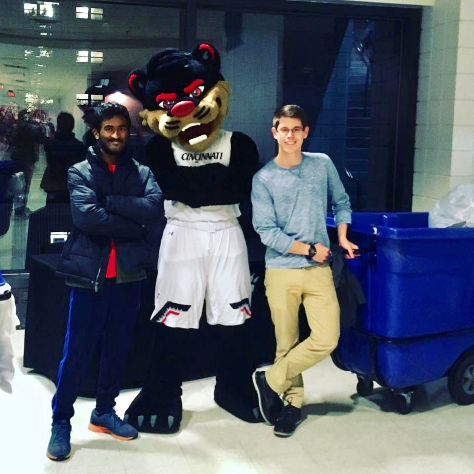 Two students stand with UC's Bearcat and a recycling can.