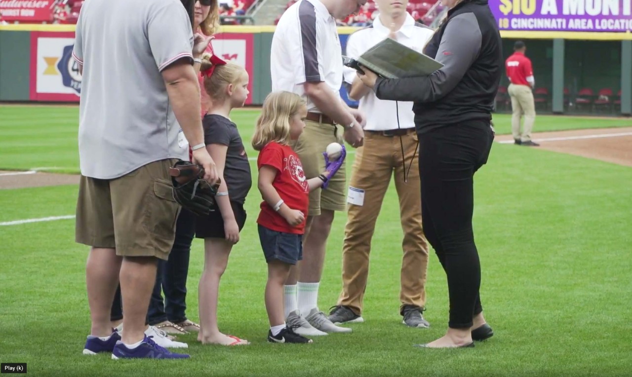 Ella Morton stands holding a baseball amid a group of adults.
