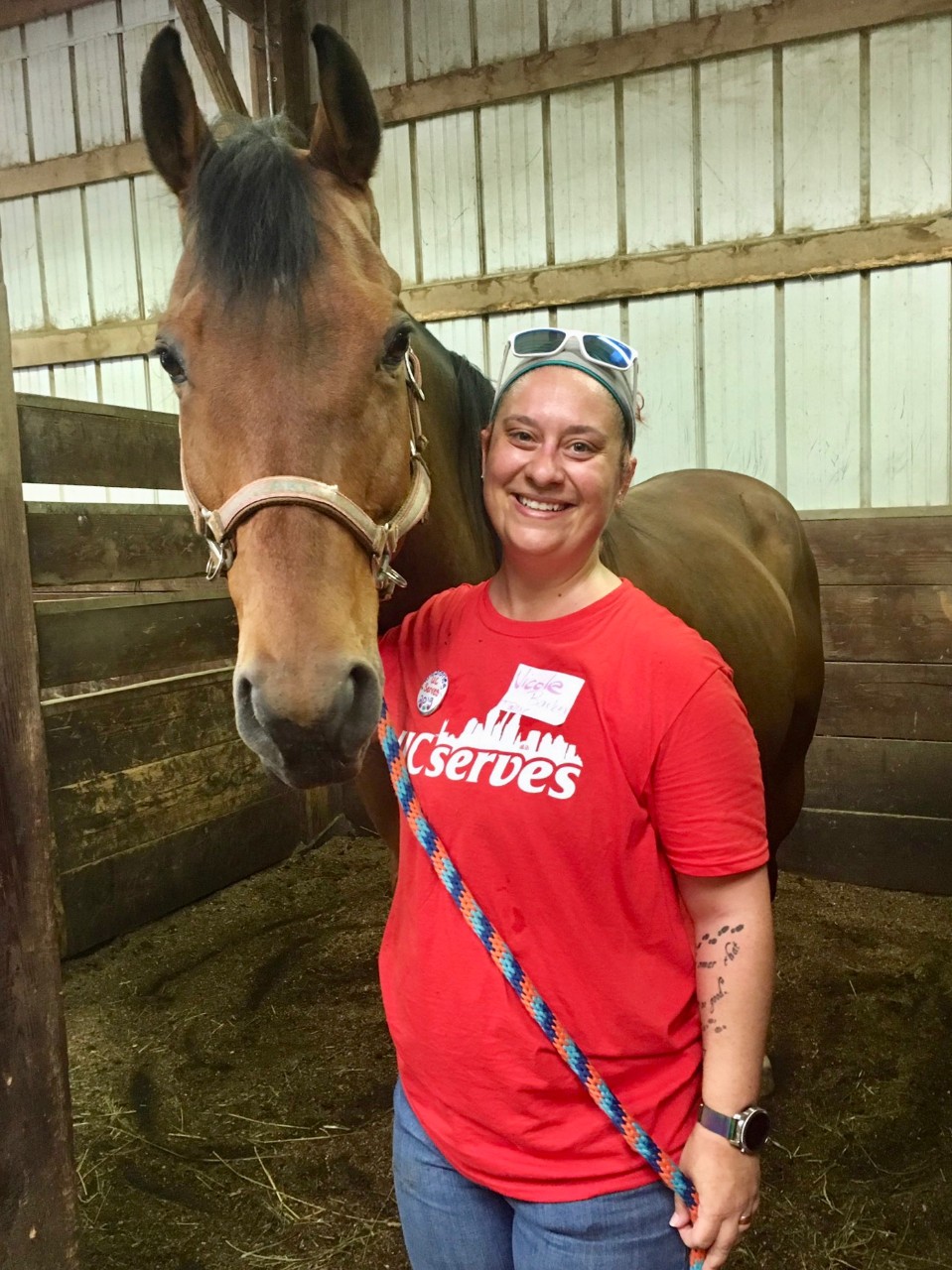 A woman stands nect to a horse in a barn.