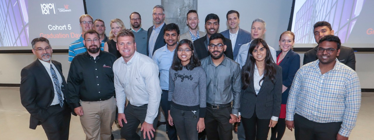 About 20 adults in business casual stand in front of two video projector screens