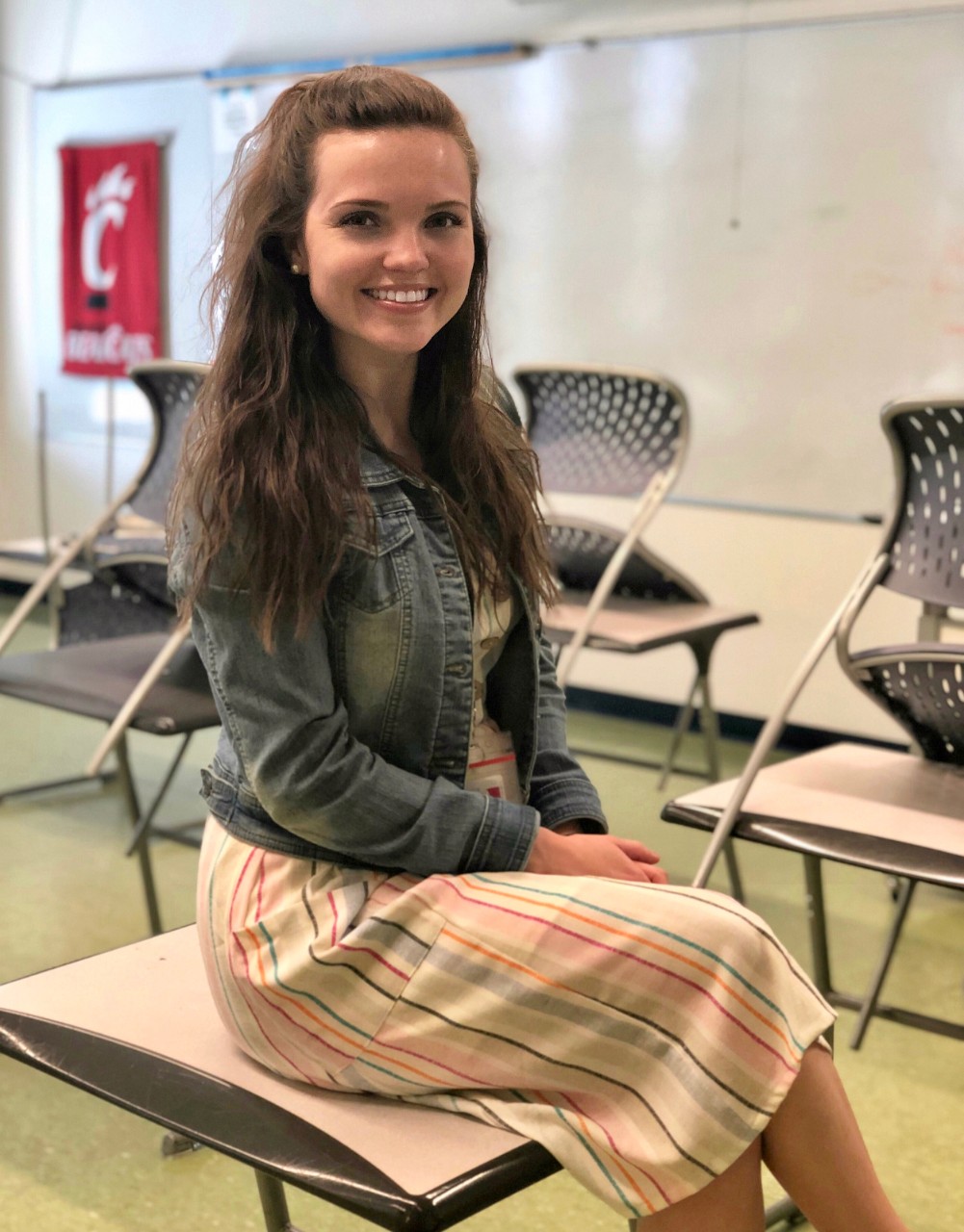 Amanda Bright, UC student in CECH sits on a desk in a classroom.