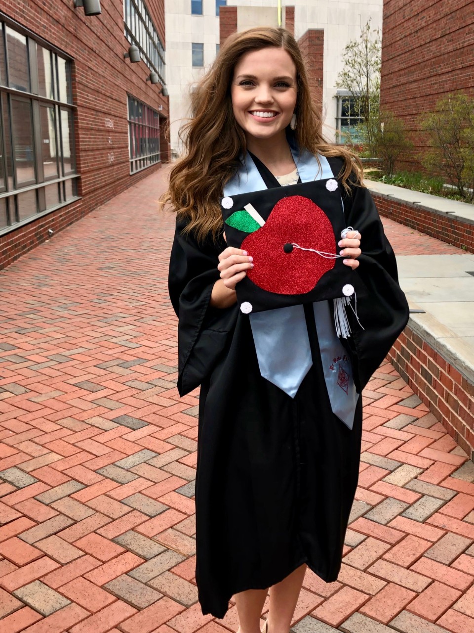 Amanda Bright, UC CECH grad, holds her graduation cap to show the teacher's apple design she created on the top.