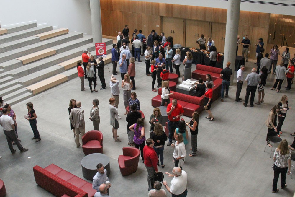 Approximately fifty people stand around and talk in a large atrium