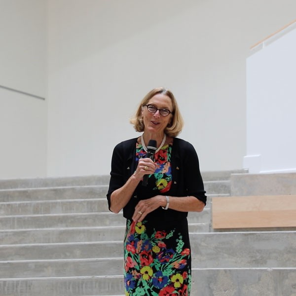 Woman in dress and sweater stands on stairs with microphone