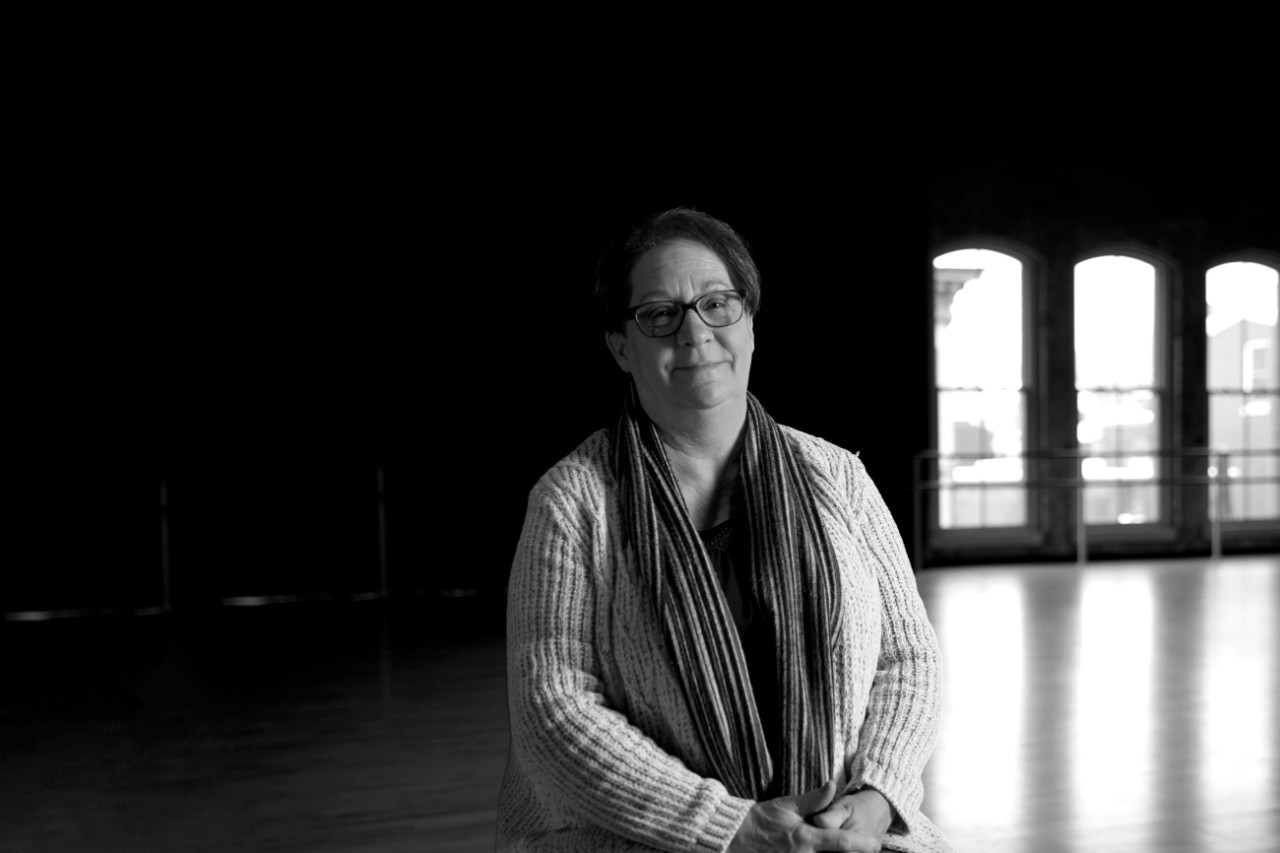A woman sits in front of a brick wall and arched windows