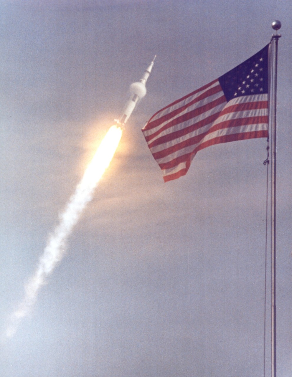 KENNEDY SPACE CENTER, FLA. - The American flag heralds the flight of Apollo 11, man's first lunar landing mission.  The Apollo 11 Saturn V space vehicle lifted off with astronauts Neil A. Armstrong, Michael Collins and Edwin E. Aldrin Jr. at 9:32 a.m. EDT from KSC's Launch Complex 39A.  During the planned eight-day mission, Armstrong and Aldrin will descend in a Lunar Module (LM) to the Moon's surface while Collins orbits overhead in the Command Module. The two astronauts are to spend 22 hours on the Moon, including two-and-one-half hours outside the LM. They will gather samples of lunar material and will deploy scientific experiments that will transmit data about the lunar environment.  They will rejoin Collins in the Command Module for the return trip to Earth.