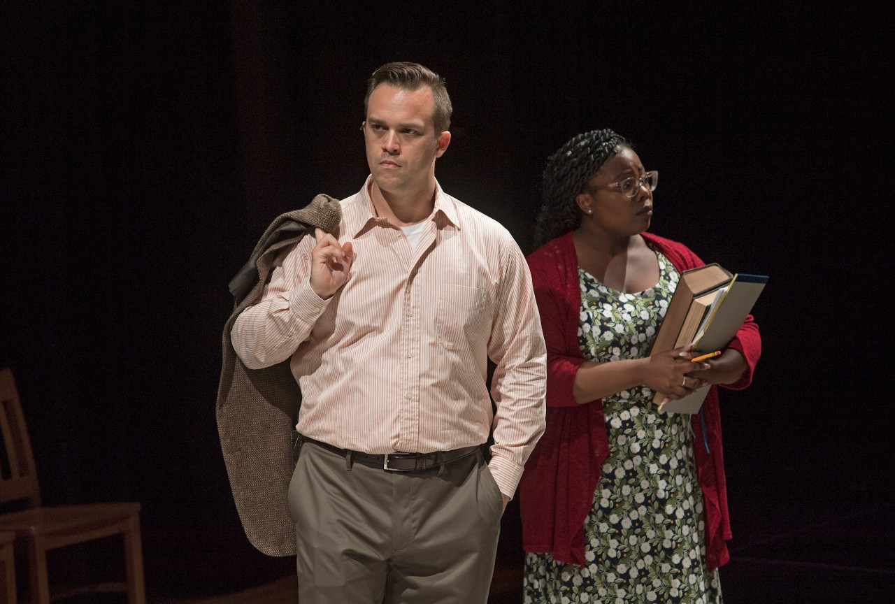 Stage scene shows man and women standing and looking in different directions