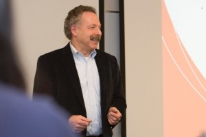 Larry Gales stands by a screen showing part of a slide with UC branding elements.