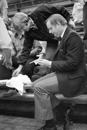 Neil Armstrong sits in bleachers folding a paper airplane.