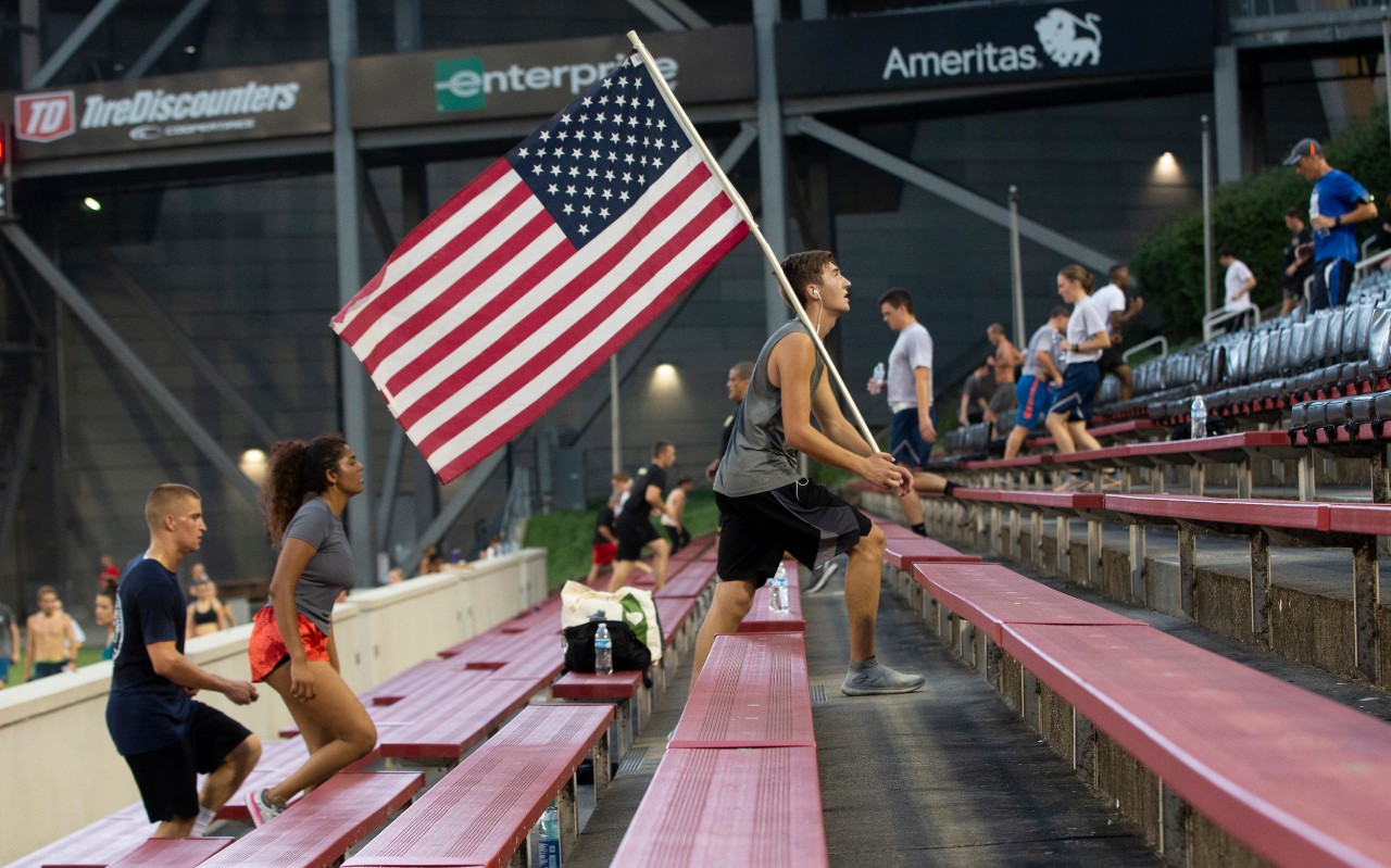 A male student runs up the stairs carrying the American flag