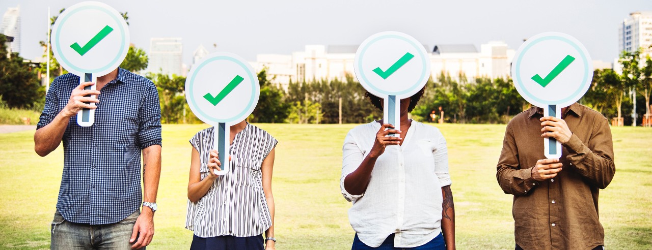 Four people holding checkmark signs over their faces