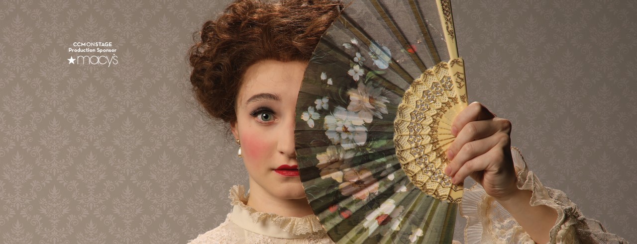 A woman with a surprised look holds a fan to partially cover her face.