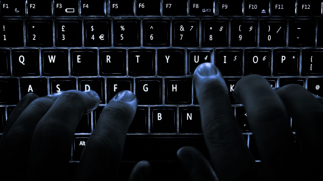Hands type on a backlit keyboard.