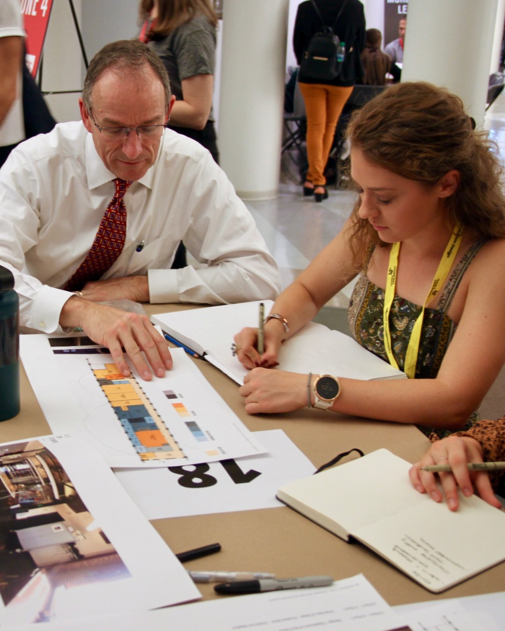 Man sits at table with DAAP students looking at schematics.