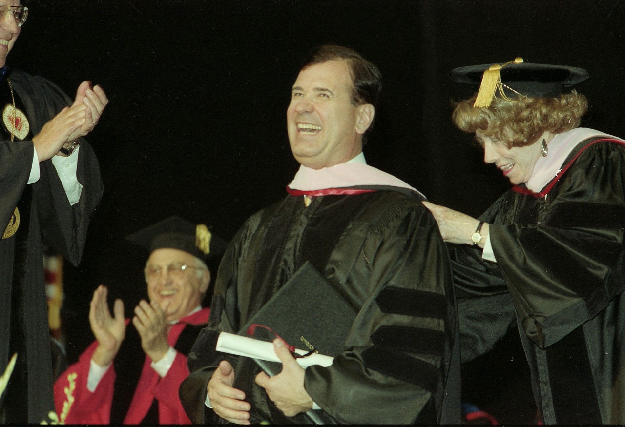 A woman hoods a man at a graduation ceremony