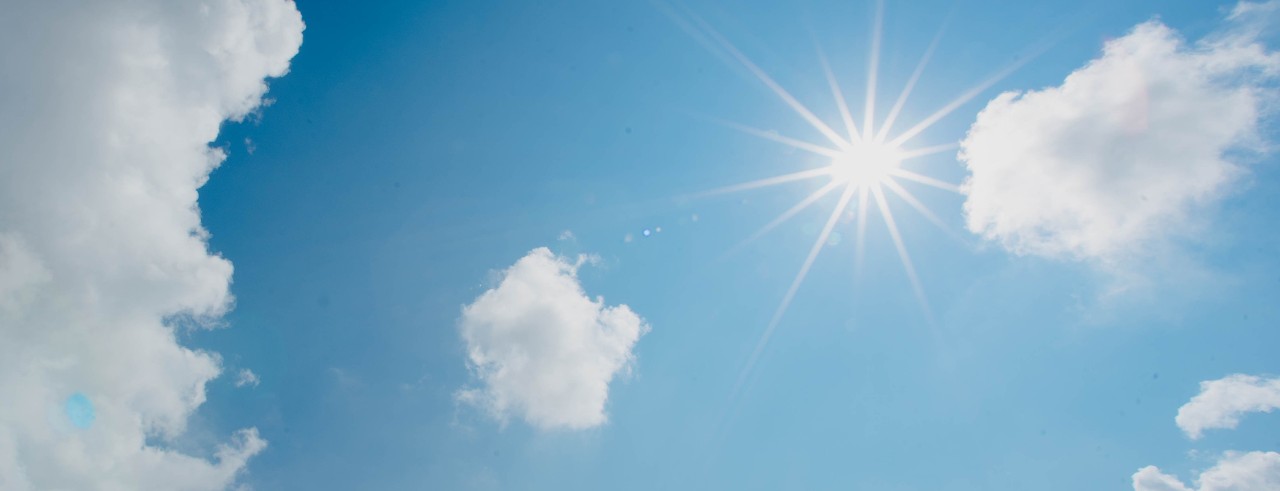 Sun shining with white clouds and blue sky.