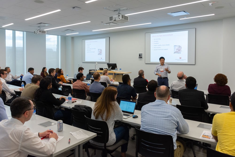adults sit in a large classroom watching a presentation on data analytics